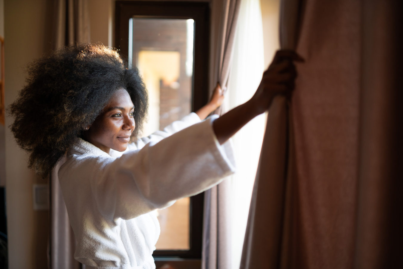 Woman pulling curtains in hotel room